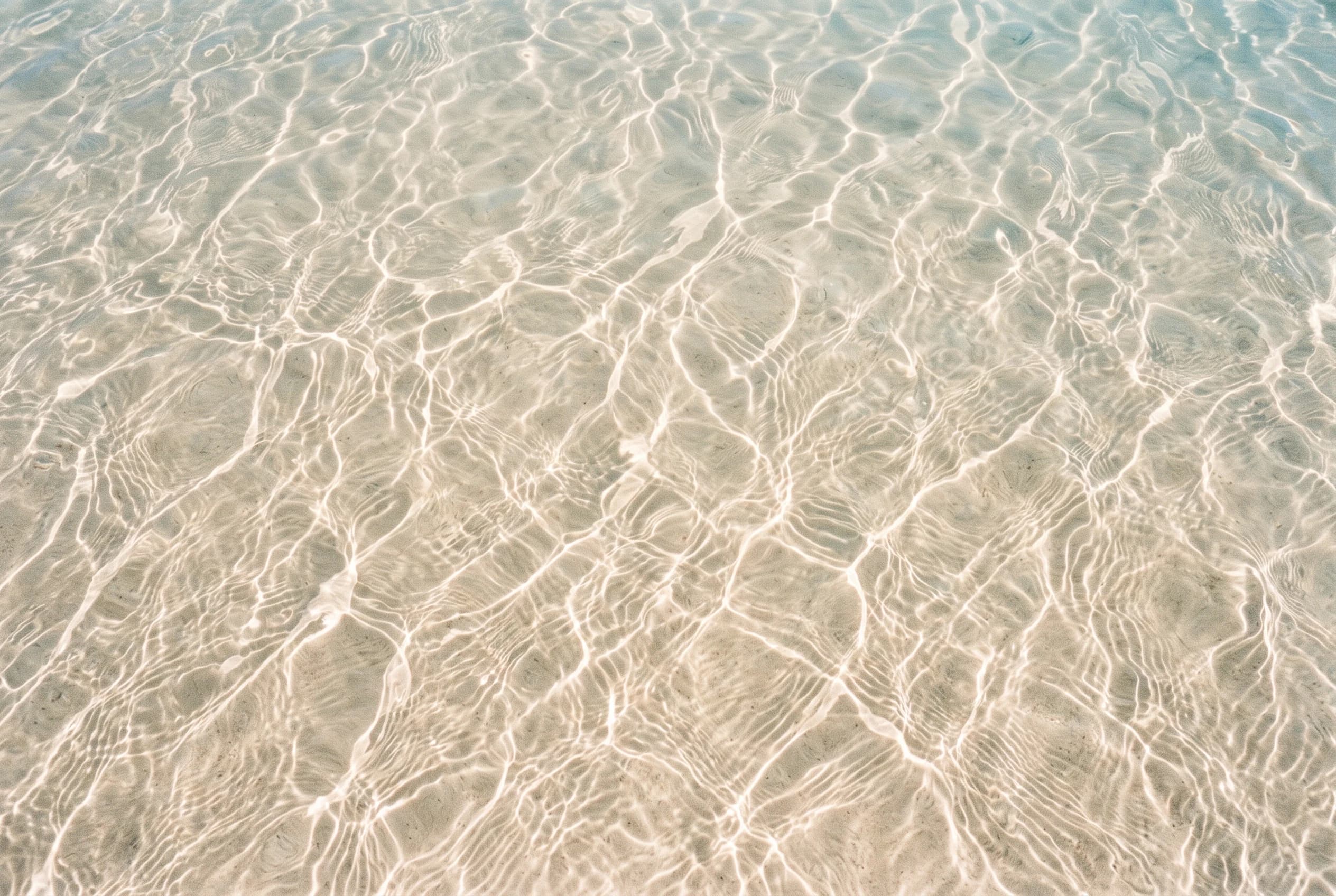 Sunlight through clear shallow water, a net of bright lines moving over pale sand
